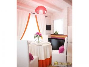 белая кухня в деревянном доме, акценты оранжевого цвета: низ скатерти, оторочка на шторах, светильник. стулья накрыты белыми чехлами, курглый стол - белой скатертью