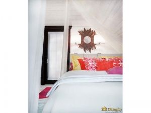 большая белая кровать на фоне белых стен. желтые, оранжевые, розовые подушки на фоне белого покрывала